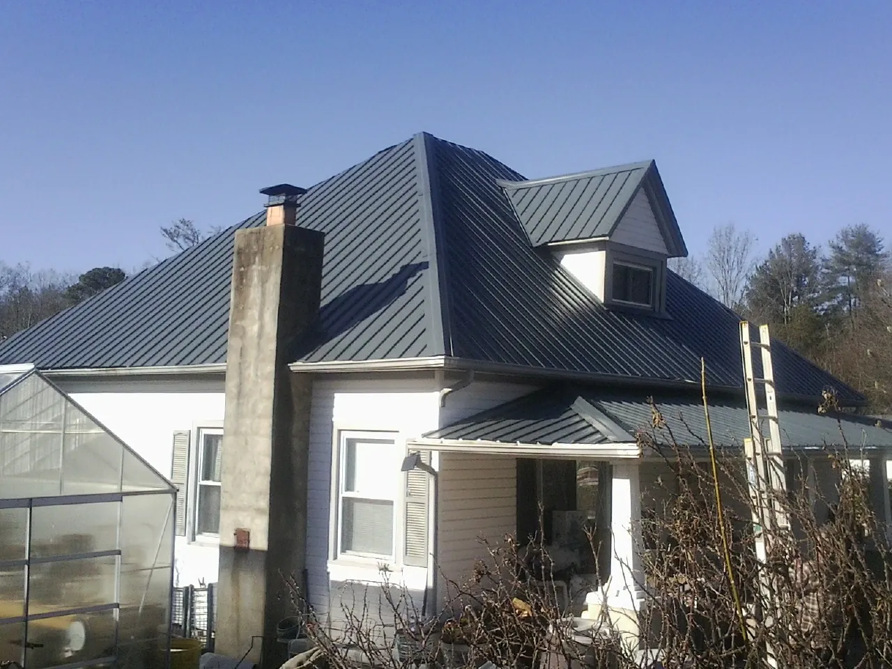Dark blue standing seam metal roof on a white farmhouse with dormer — Slate & Tile Roof Repair by Roofing Brothers in Leadore