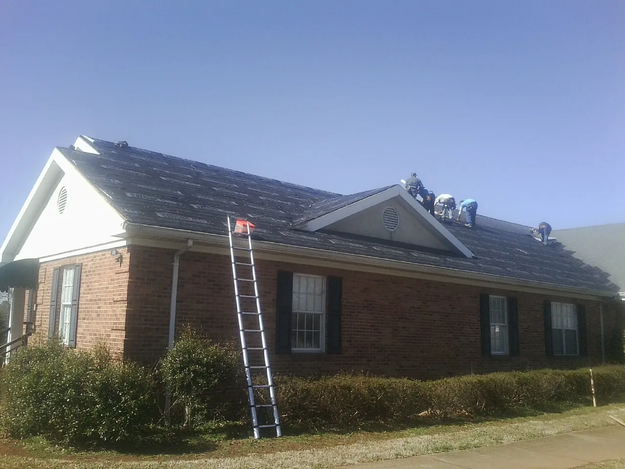 Crew tearing shingles off a brick ranch roof with a ladder set — Emergency Roof Repair work by our crew in Leadore