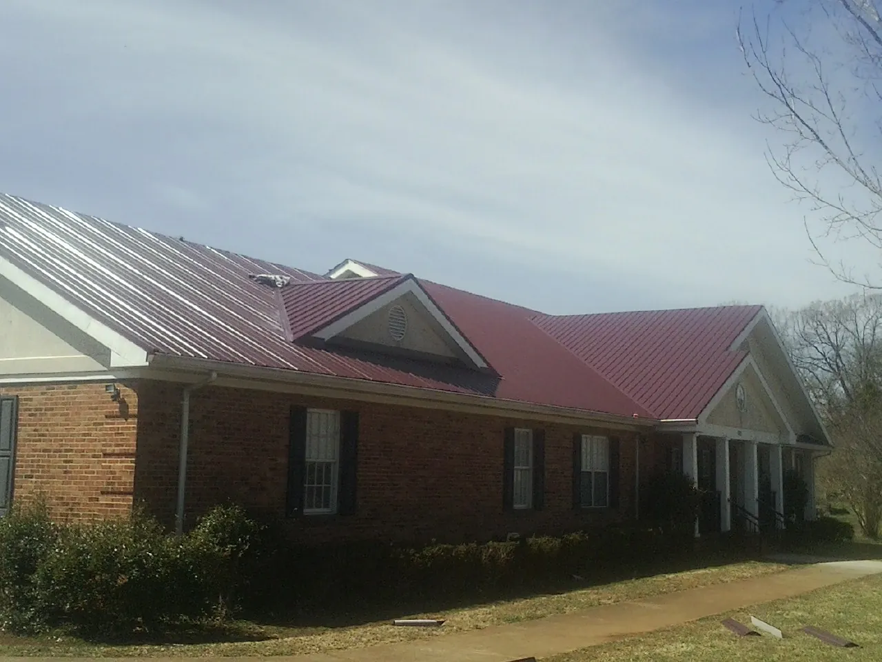 Red metal roof with gabled entries on a long brick building, from a Hail Damage Roof Repair job in Leadore