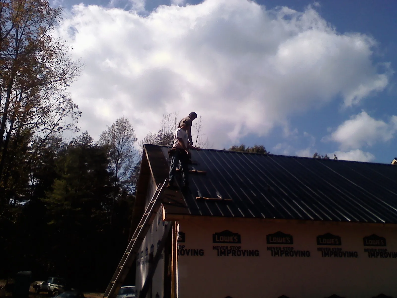 Roofer fastening dark metal panels high against a cloudy sky, from a Roof Inspection job in Leadore