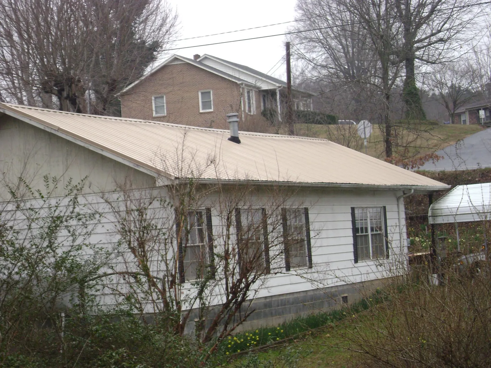 Tan metal roof on a white sided house set into a hillside — Commercial Roofing by Roofing Brothers in Leadore